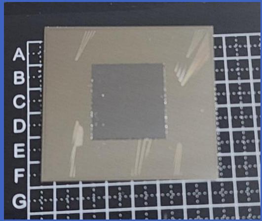 Close-up of a square electronic component with internal traces, placed on a grid background (no visible text or symbols)